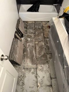 Bathroom with a damaged floor, exposed subflooring, and a bathtub at the back.