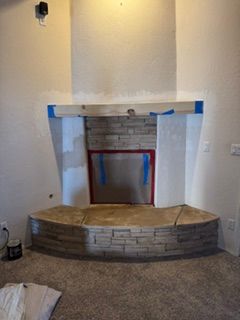 Empty brick fireplace with a curved stone hearth in a beige room, taped for renovation