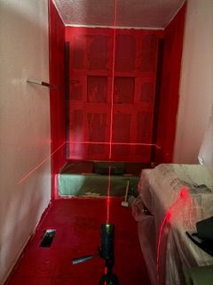 Red-painted hallway with a green floor, a black fixture in the foreground, and a covered object on the right.