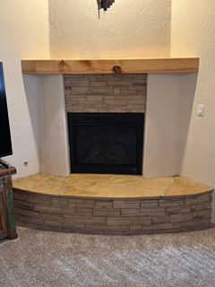 Stone fireplace with black insert, wood mantel, and carpeted hearth in a living room