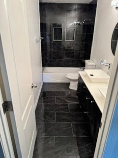 Narrow bathroom with black tile, white sink vanity, toilet, and shower at the far end