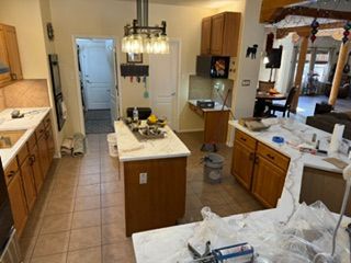 Bright kitchen with two islands, white countertops, wood cabinets, and a dining area beyond.