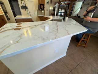 Large white marble kitchen island with a cup, in a tiled kitchen; person seated at right edge