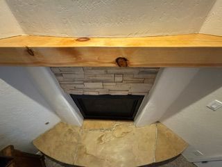 Ceiling view of a room with a wooden beam, stone fireplace opening, and a tan stone hearth