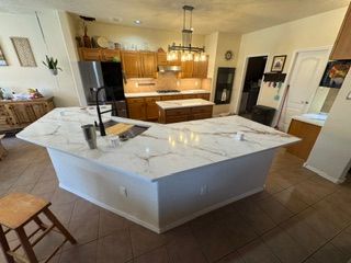 Modern kitchen with large white marble island, wood cabinets, and tiled floor