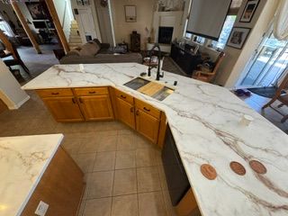 Curved kitchen island with white marble-look countertop, wood cabinets, and tan tile floor in a home interior