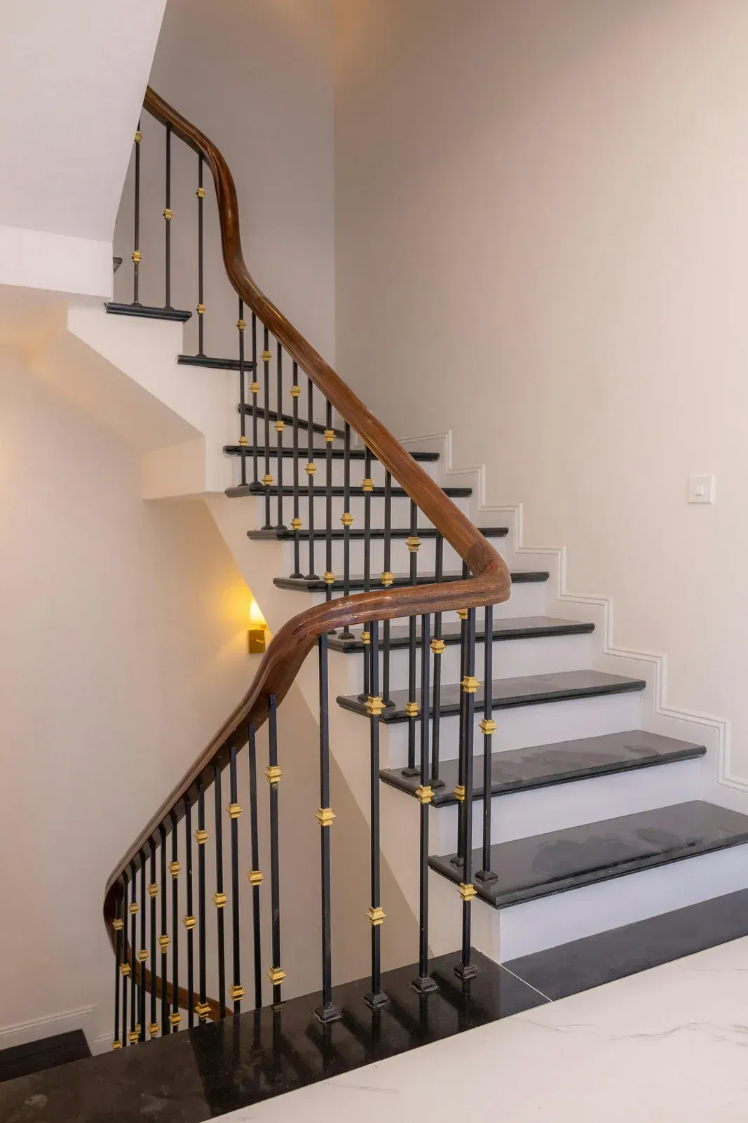 Curved staircase with dark steps, black metal spindles, and a brown wooden handrail against a white wall.
