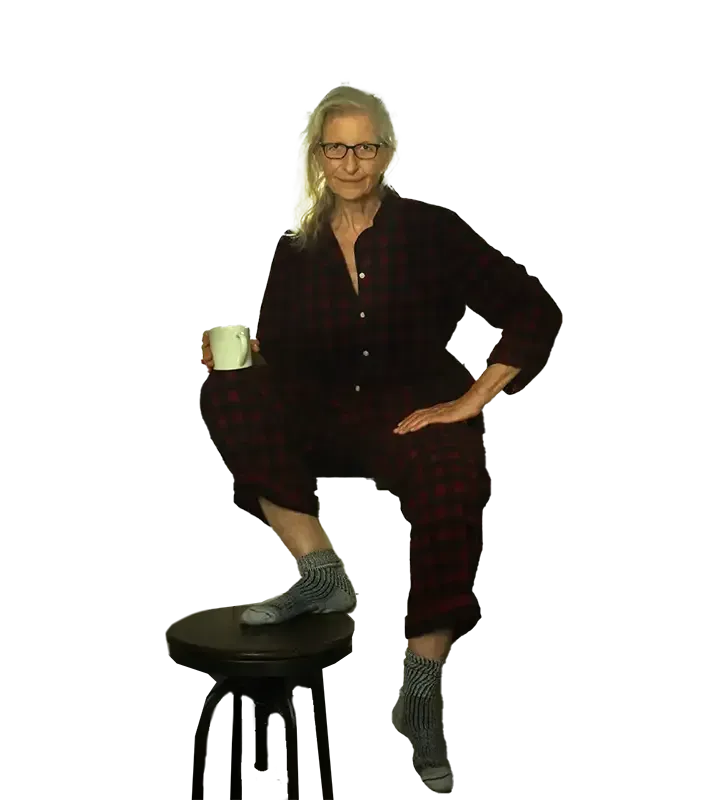 A woman in pajamas is sitting on a stool holding a cup of coffee