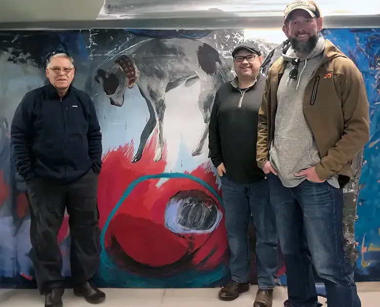 Three men standing in front of a painting of a dog