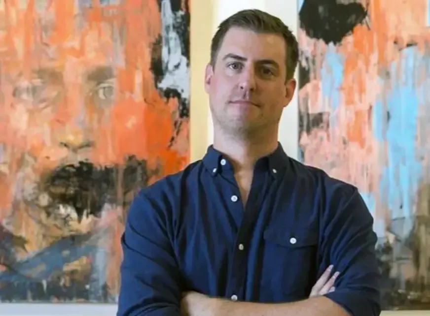 A man is standing in front of a painting with his arms crossed.