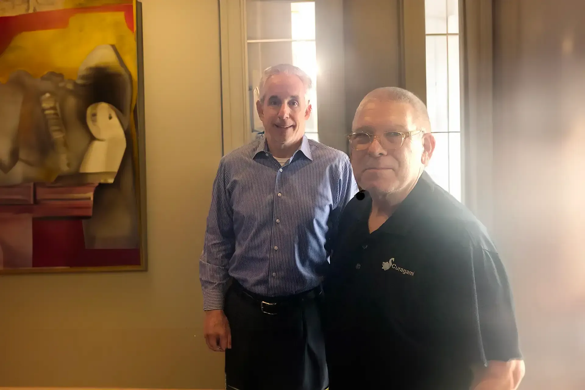 Two men are posing for a picture in front of a painting