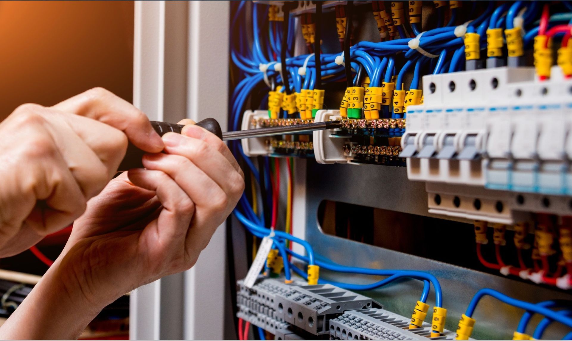 Hands using a screwdriver on electrical wiring in a breaker box.