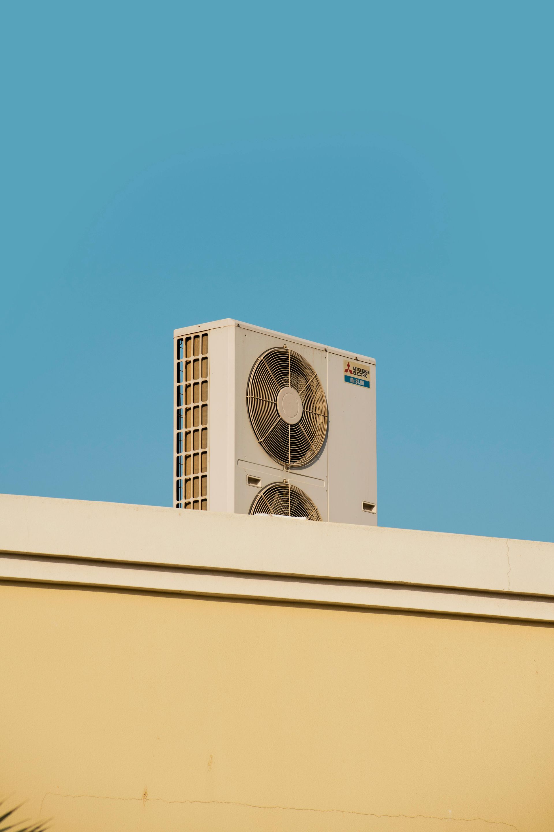 White air conditioner on a beige wall against a clear blue sky.