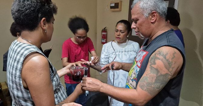 People in a room, one with a tattoo, holding a cup, likely a ceremony.