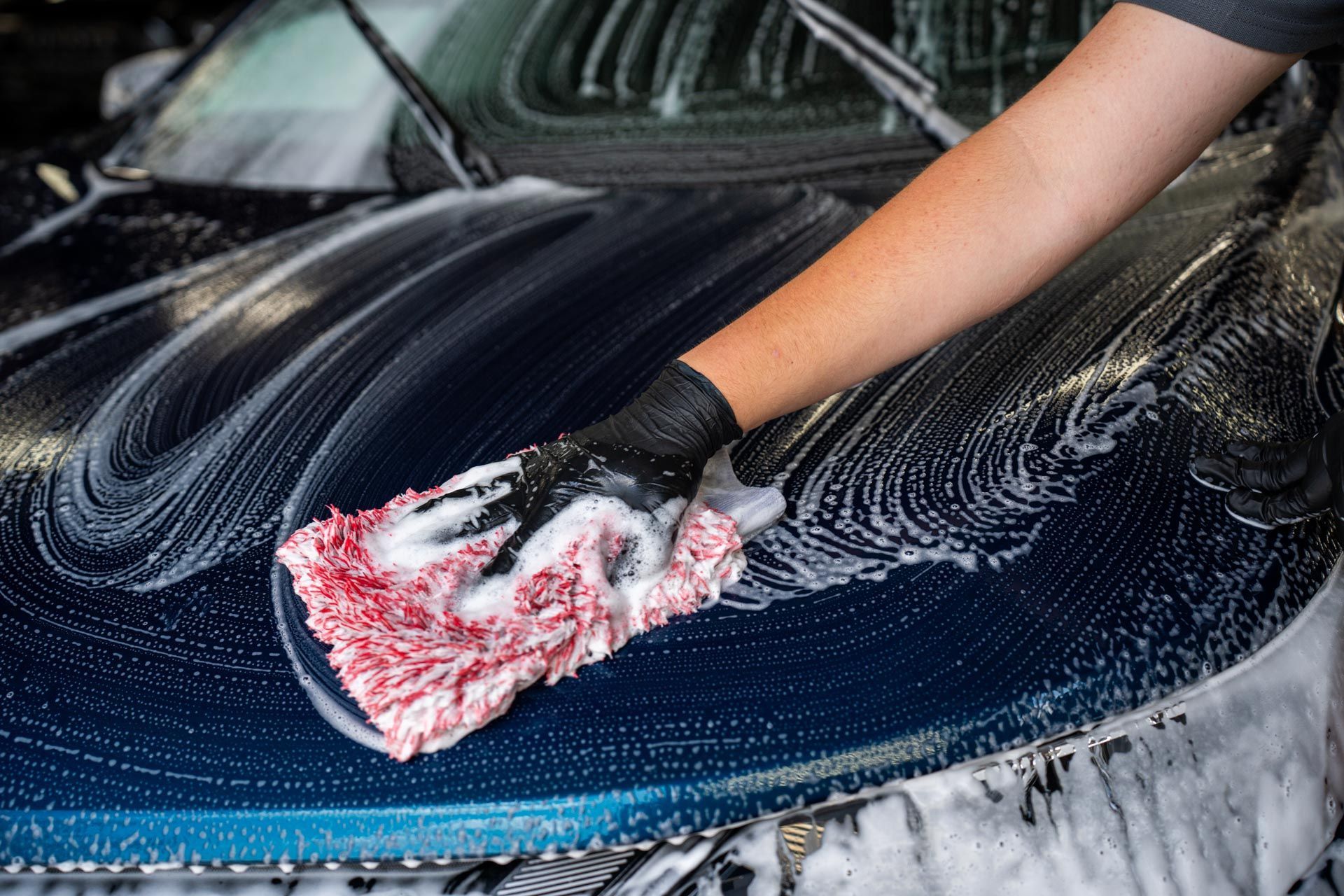 Person washing a dark blue car with a soapy wash mitt.