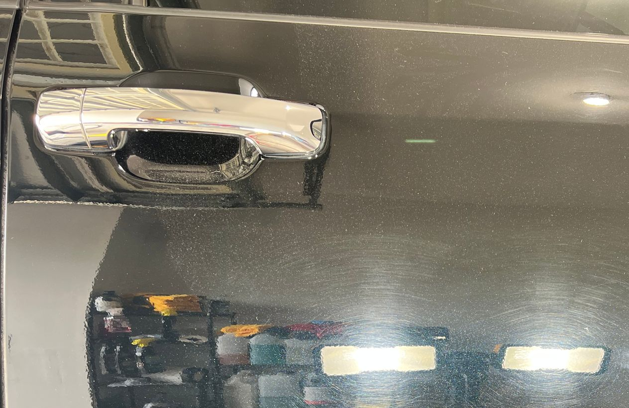 Chrome car door handle on a black car door with reflections.