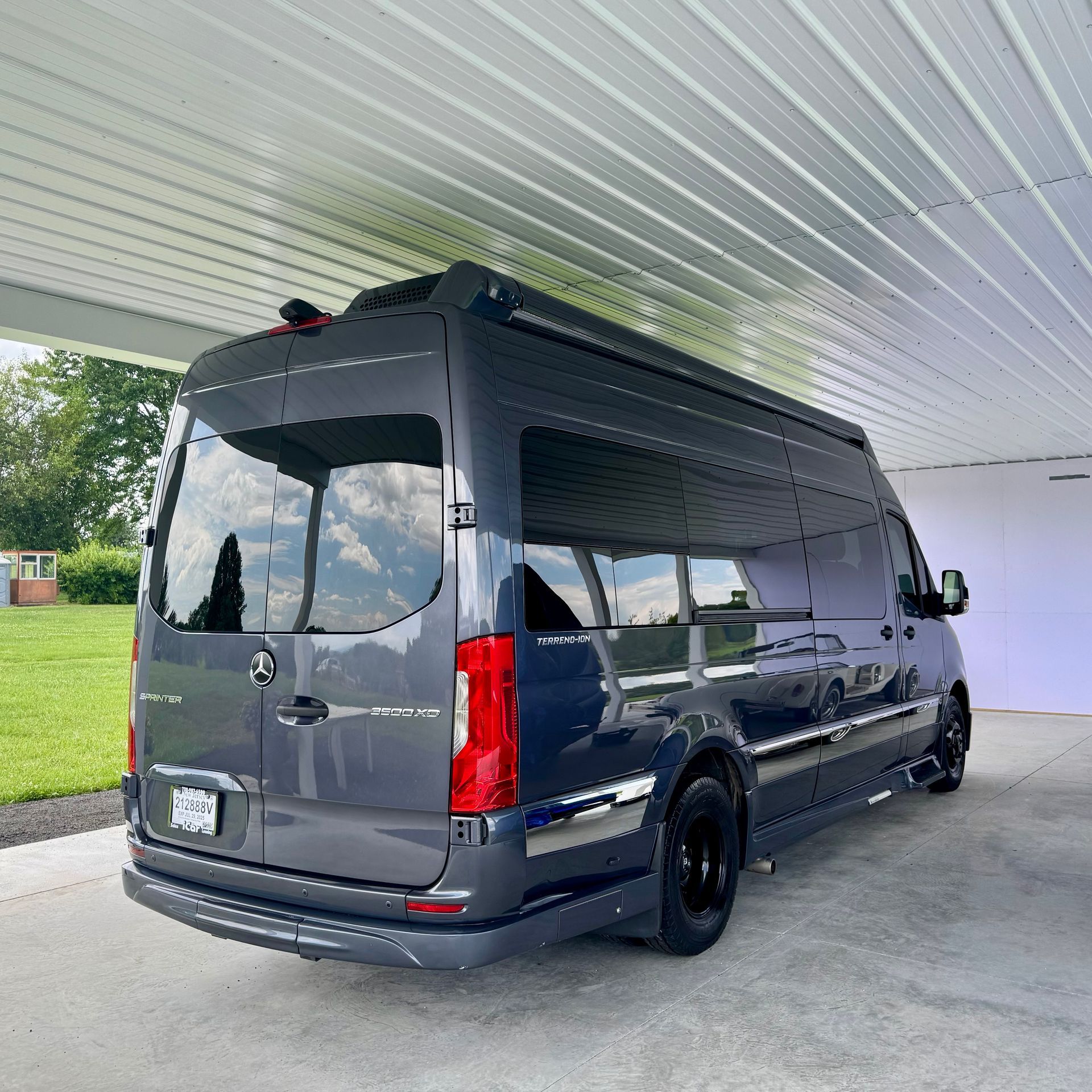 Dark gray van parked under a white awning with a green lawn in the background.