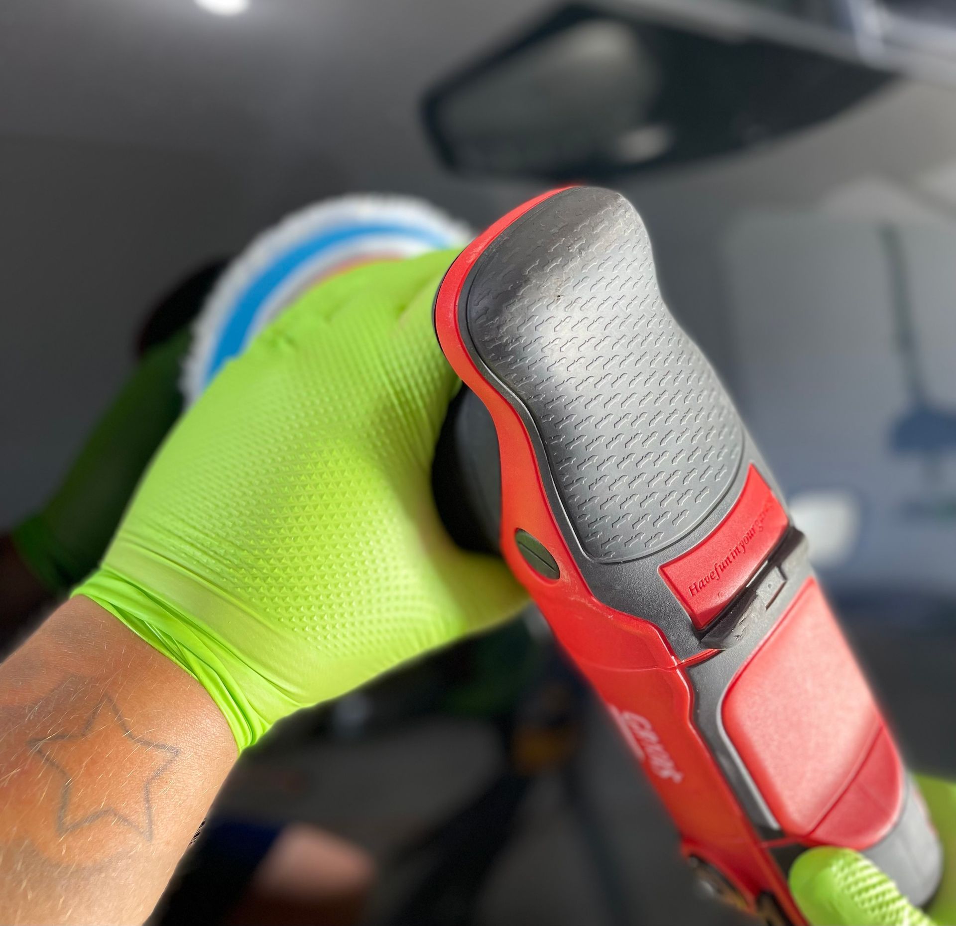 Gloved hand holding a red and black orbital polisher against a car's surface, using a white polishing pad.