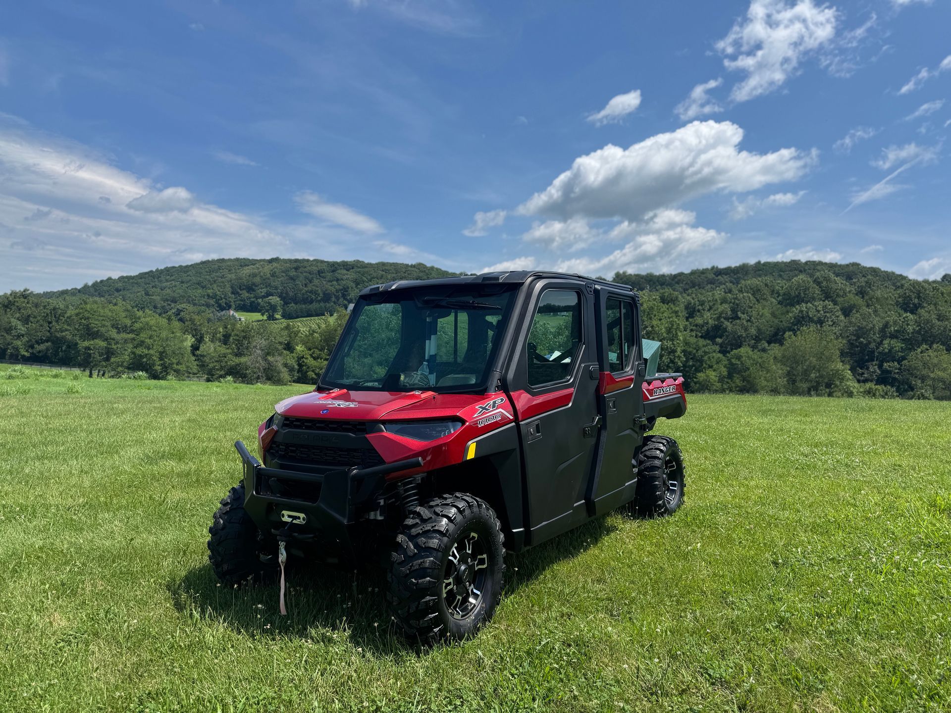Red and black UTV in a grassy field with a backdrop of trees and a blue sky.