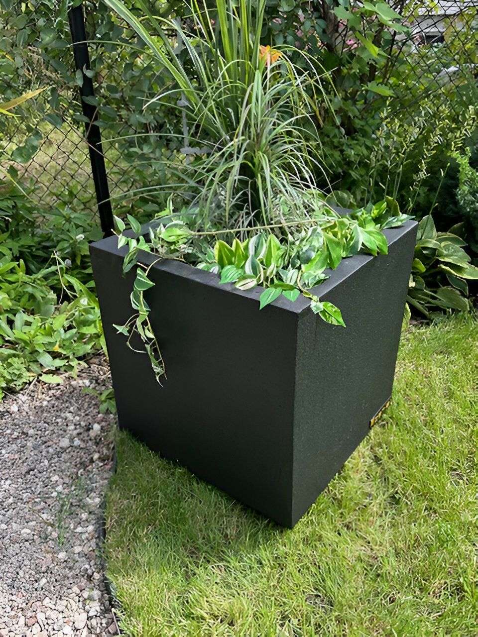 Une jardinière noire remplie de plantes est posée au sommet d'un champ vert luxuriant.