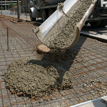 Concrete being poured from a truck chute onto a steel-reinforced foundation slab.