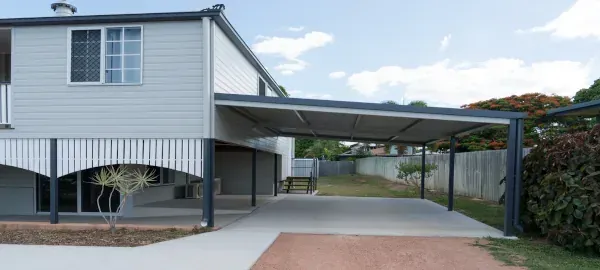 House with covered carport and driveway, showing a white exterior and brick base.