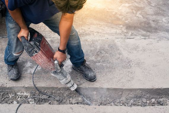 Worker using a jackhammer to break concrete pavement near a curb