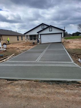 New concrete driveway leading to a white house with a double garage, under cloudy skies.