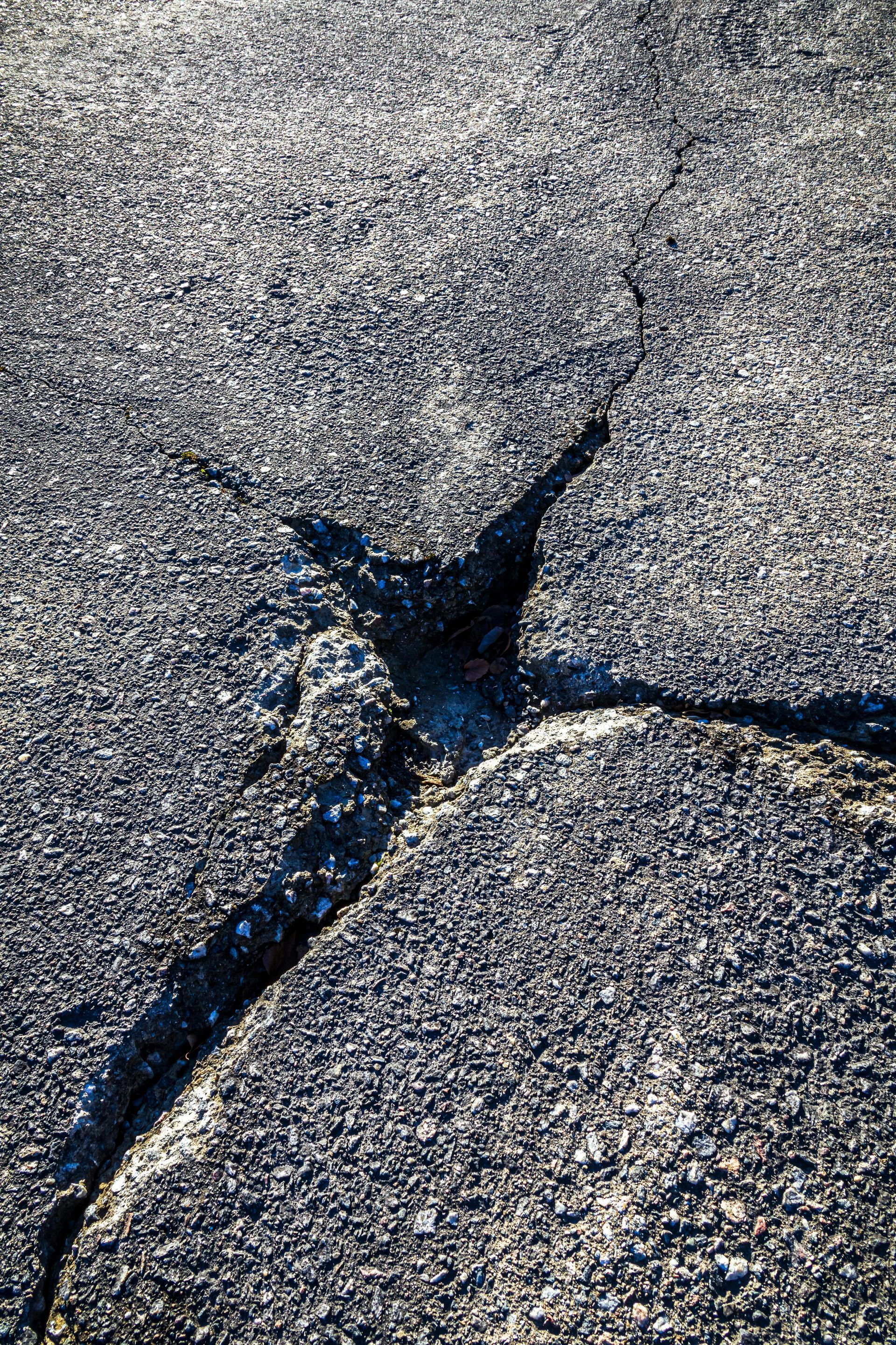 Close-up of cracked asphalt with a dark fissure branching through the pavement