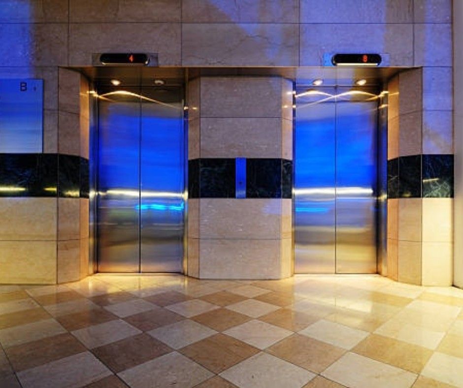 Two stainless steel elevator doors in a tiled lobby with blue lights above and a beige checkered floor