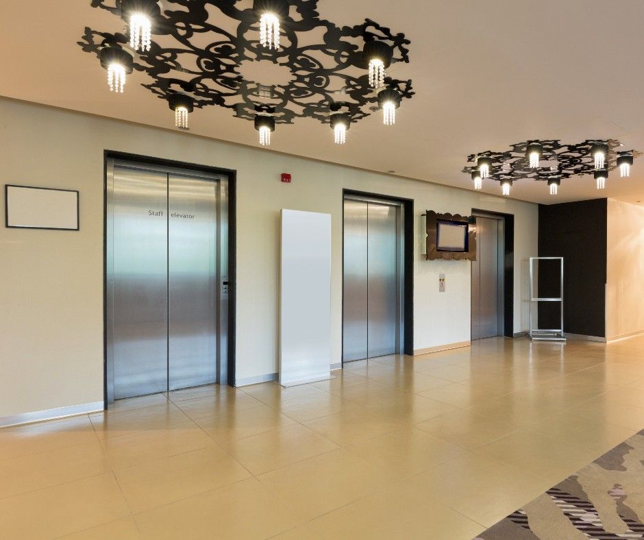 Modern lobby with elevator doors, decorative ceiling lights, beige walls, and polished floor