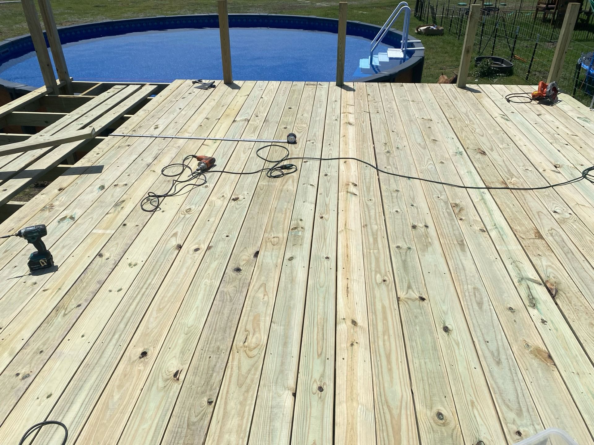 Wooden deck partially built near a blue above-ground pool. Tools and materials are visible.