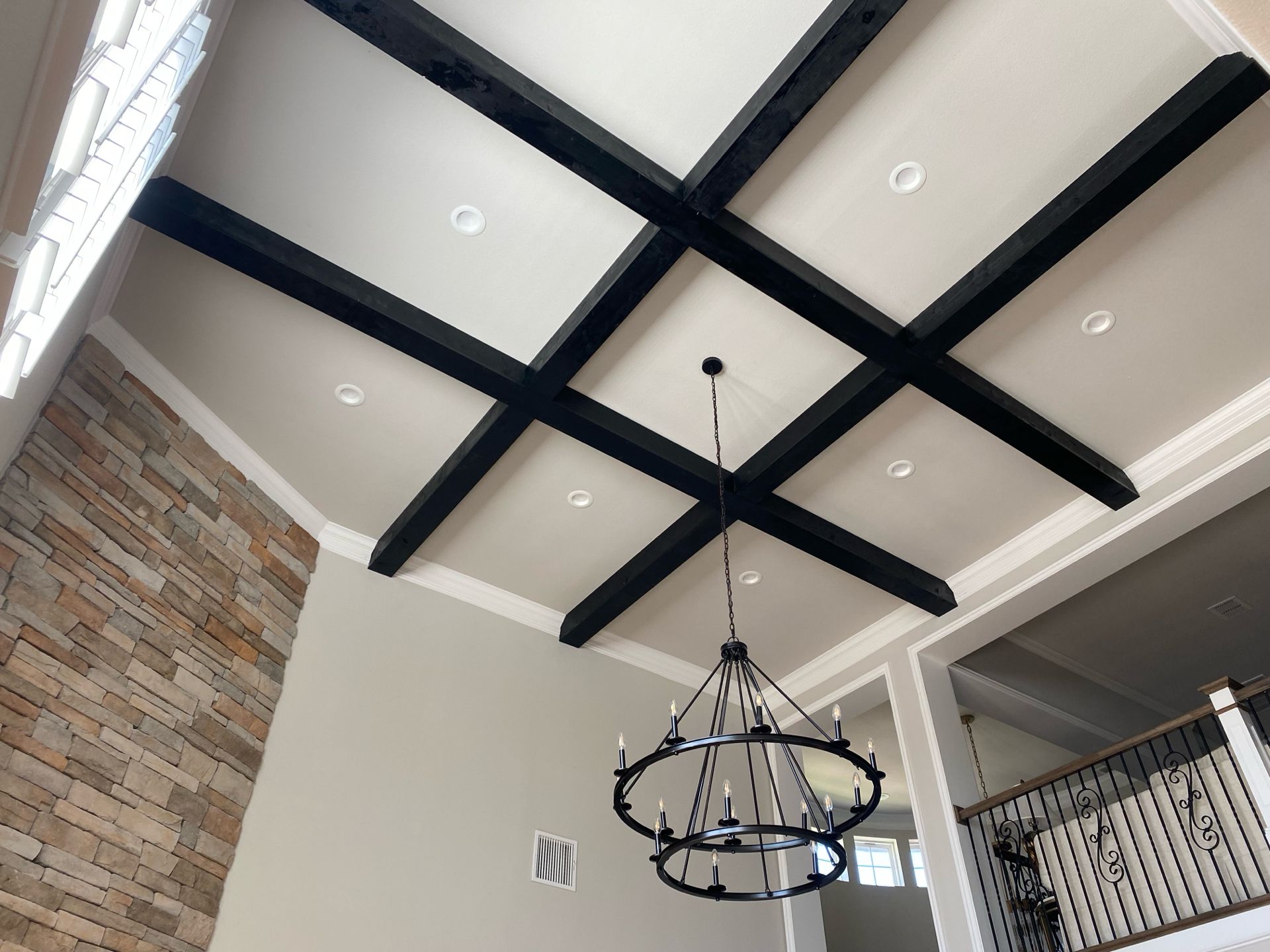 High ceiling with black beams, a chandelier, and stone accent wall.