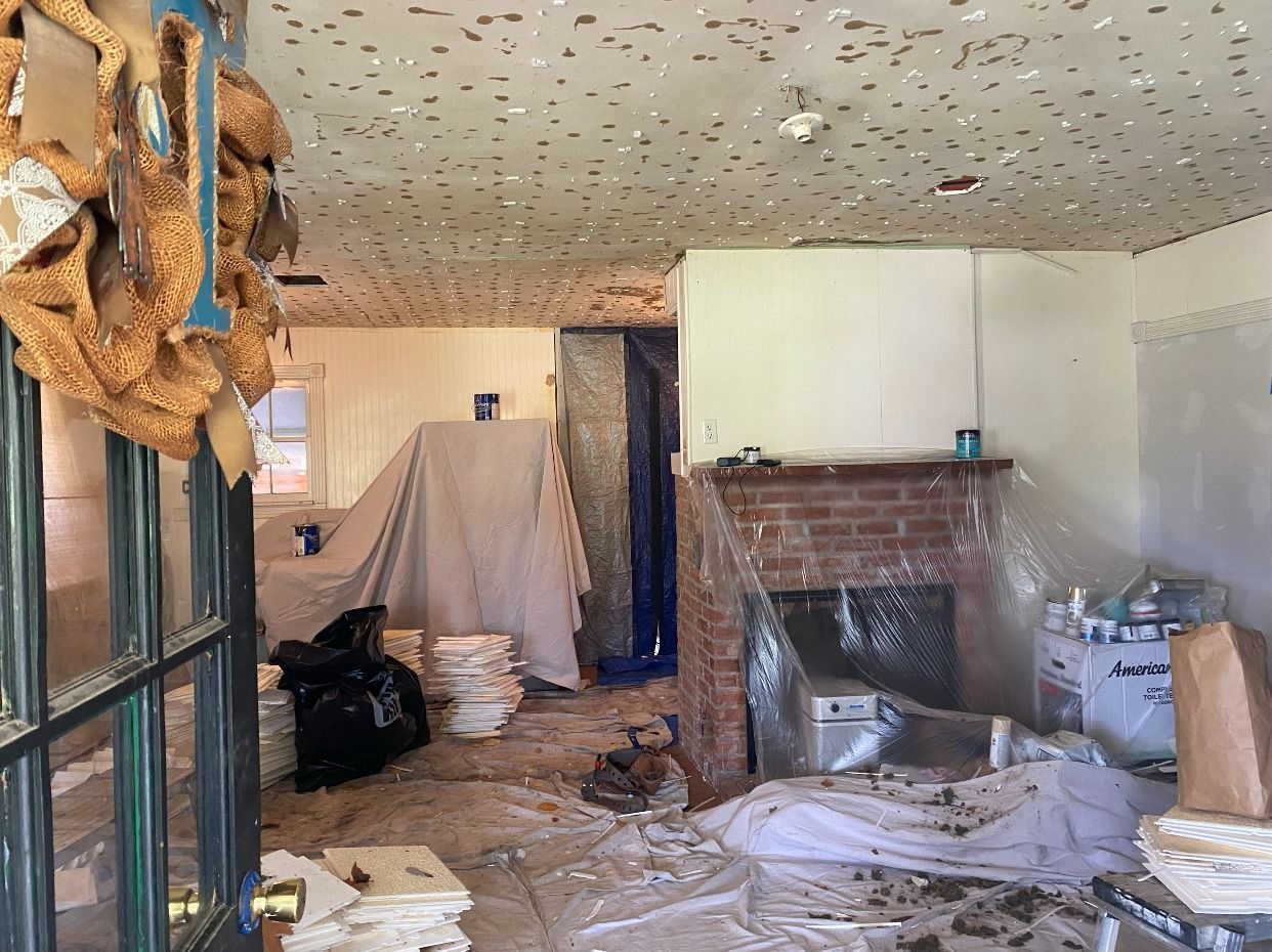 A messy interior room with debris, covered furniture, exposed ceiling, and a brick fireplace.