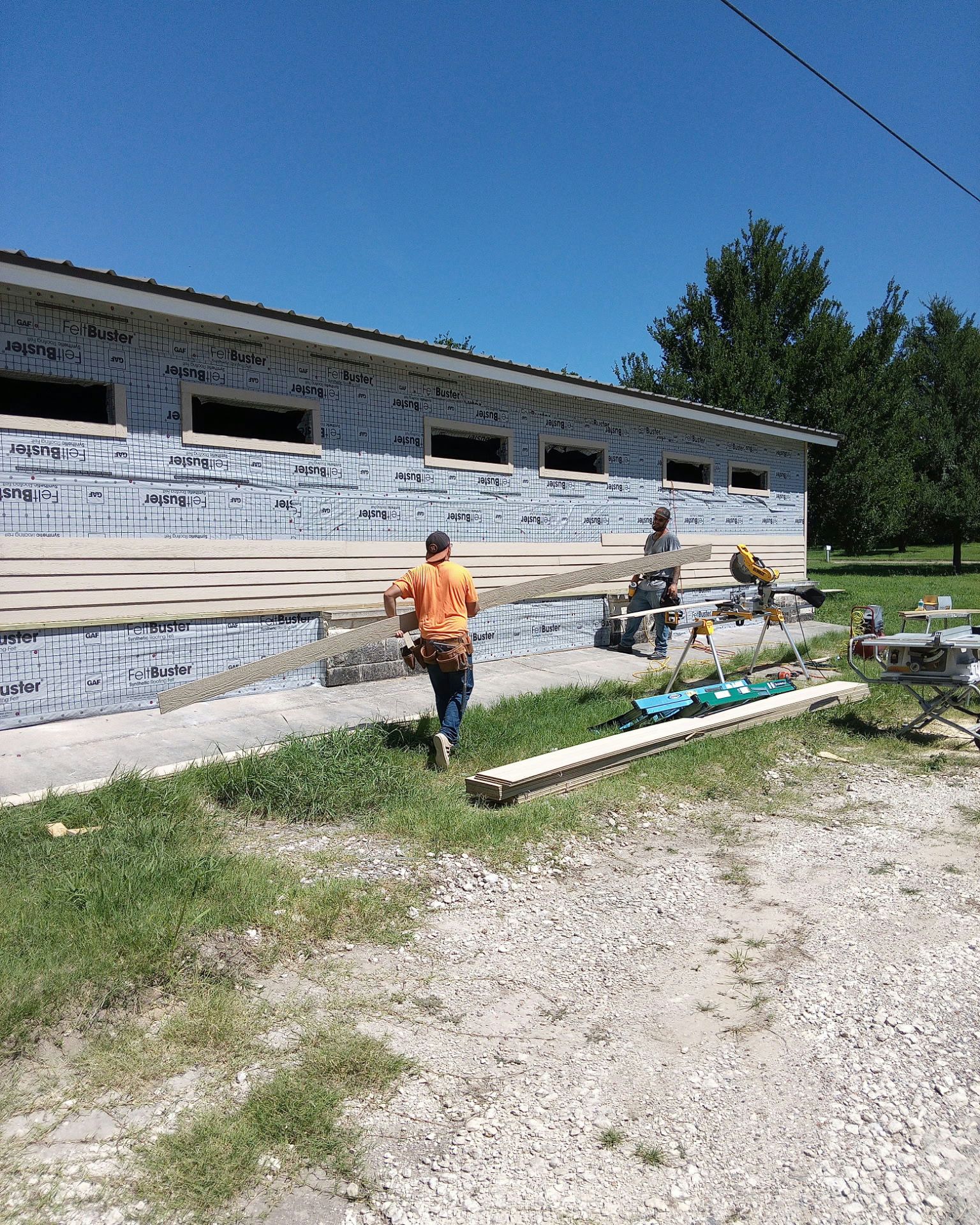 Construction workers installing siding on a one-story building, outdoors on a sunny day.