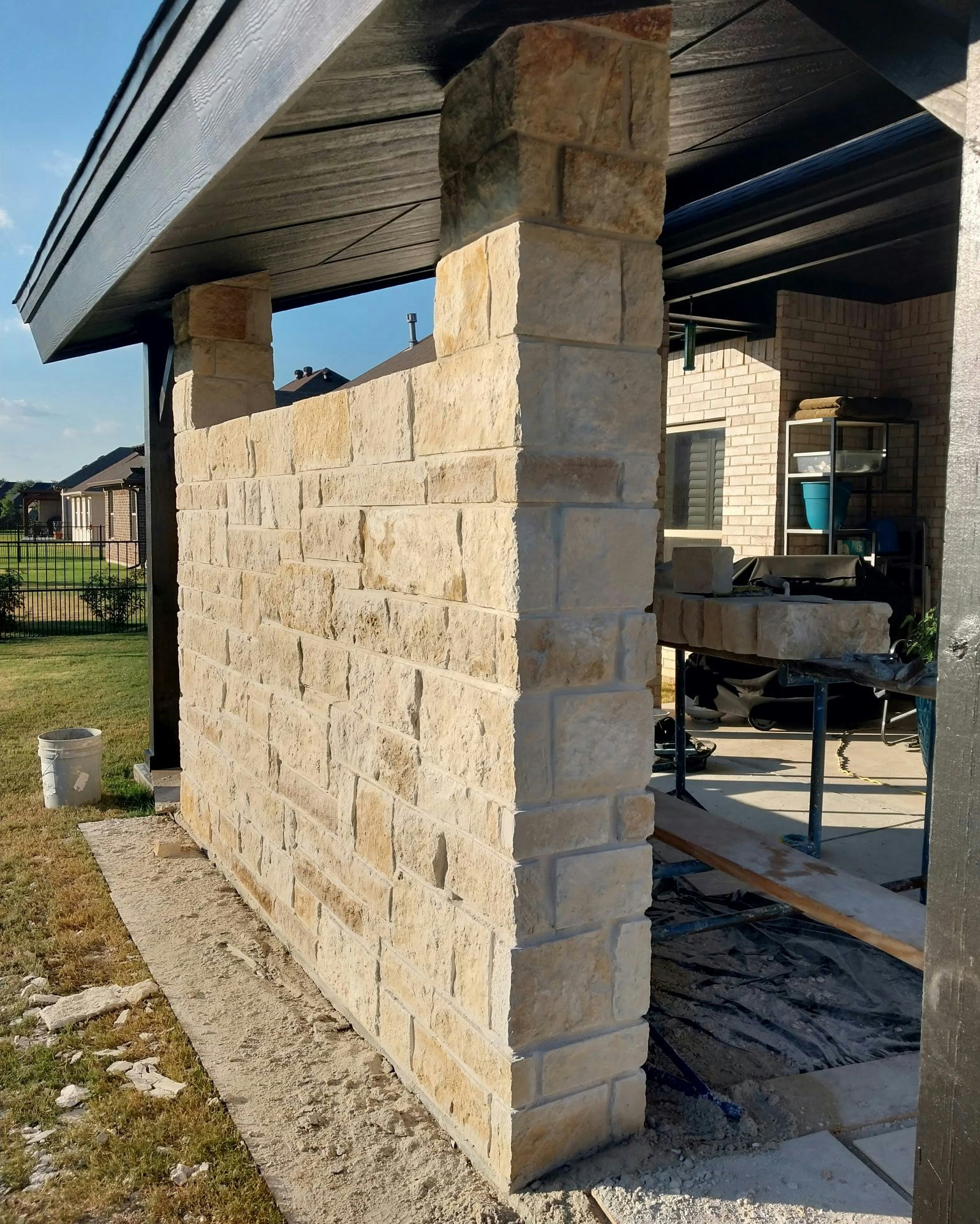 Stone wall being built under a patio cover; light-colored bricks, outdoor setting.