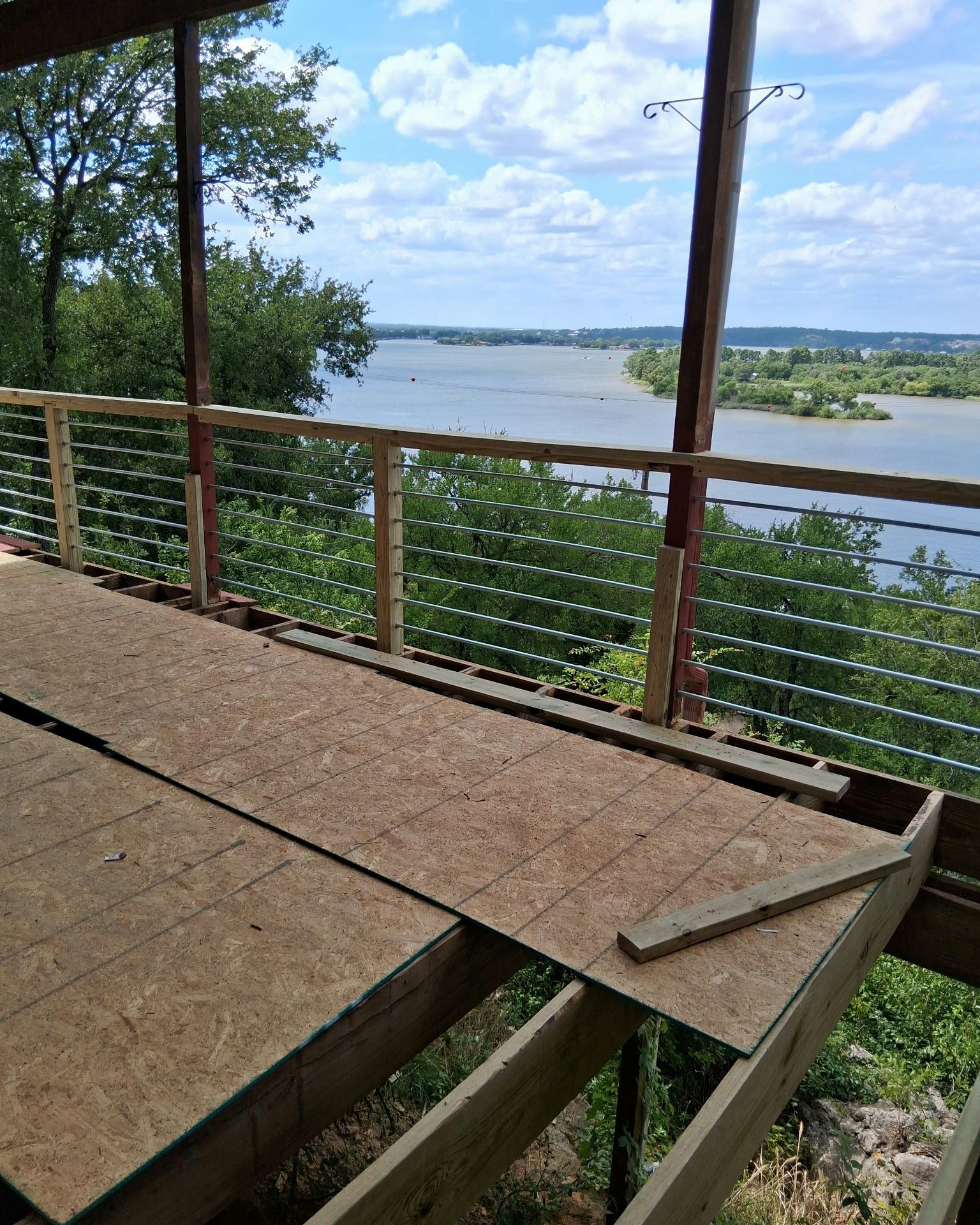 Partially constructed deck overlooking a wide river, blue sky, and green trees.