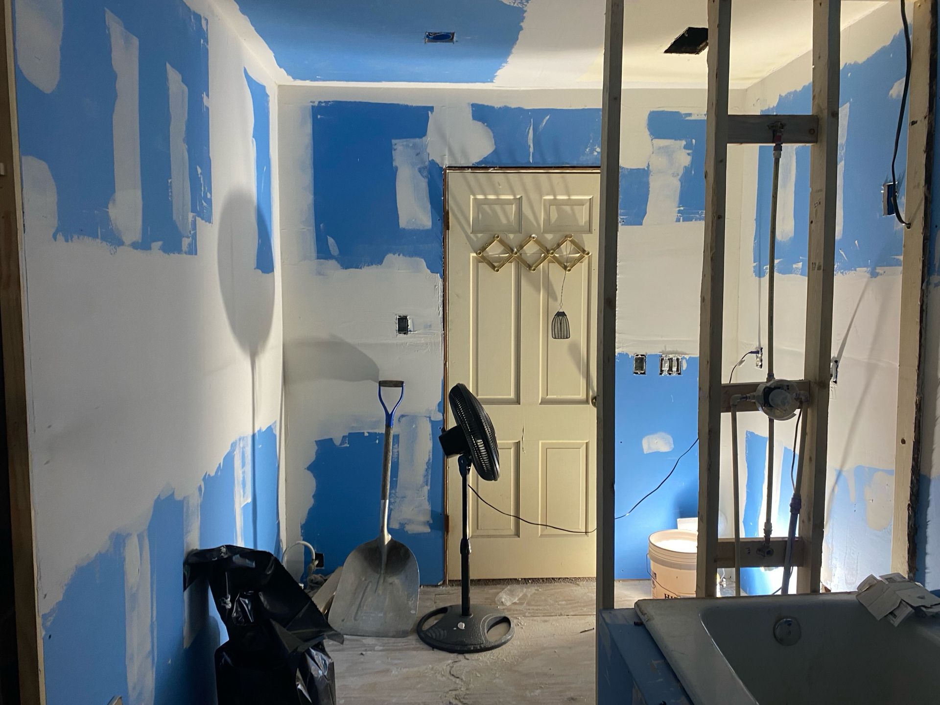 Bathroom renovation in progress. Blue drywall mudding, door, fan, and shovel.