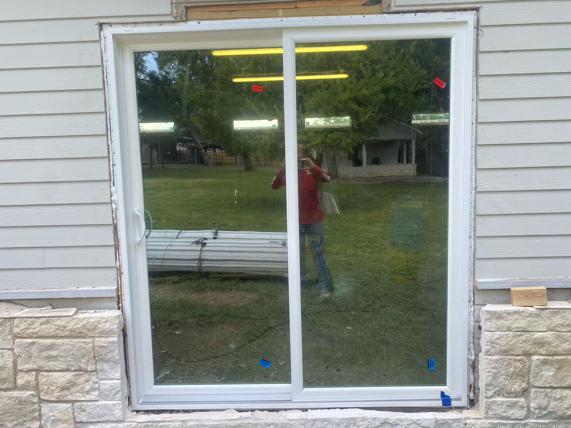 A white sliding glass door installed in a home's exterior wall, with a person reflected in the glass.