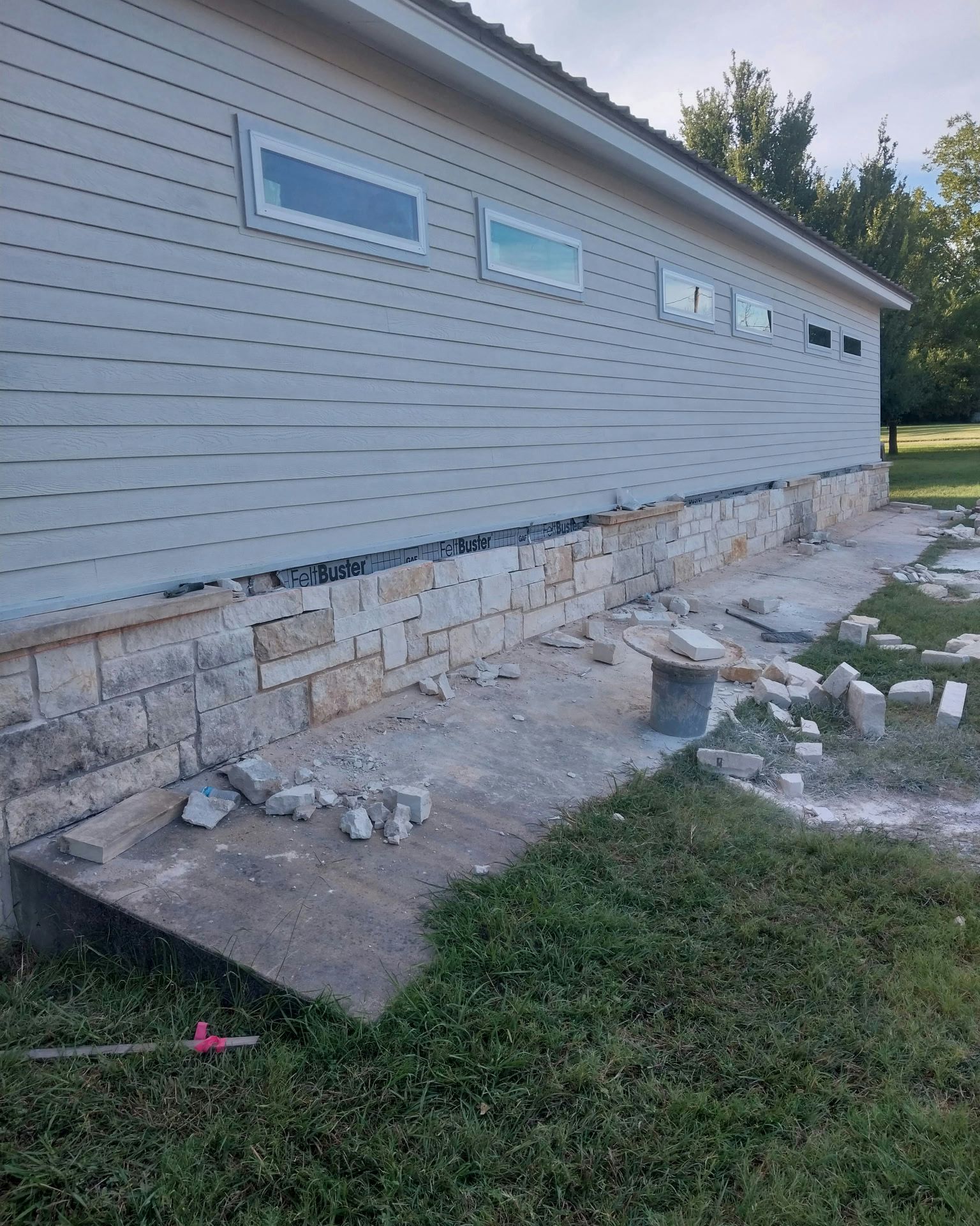 Side view of a building under construction; stone base is being built along gray siding.