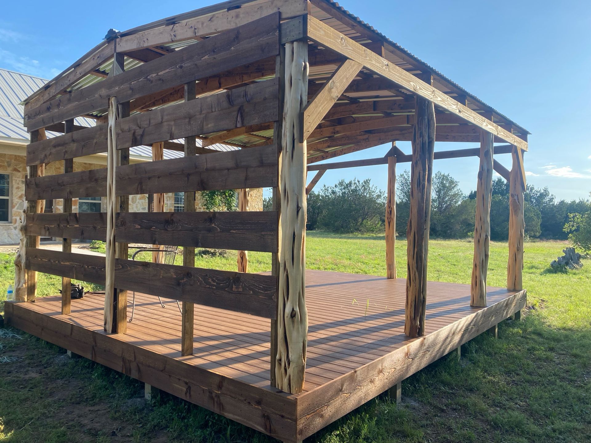 Wooden outdoor structure with a deck, horizontal siding, and open roof, in a grassy yard.