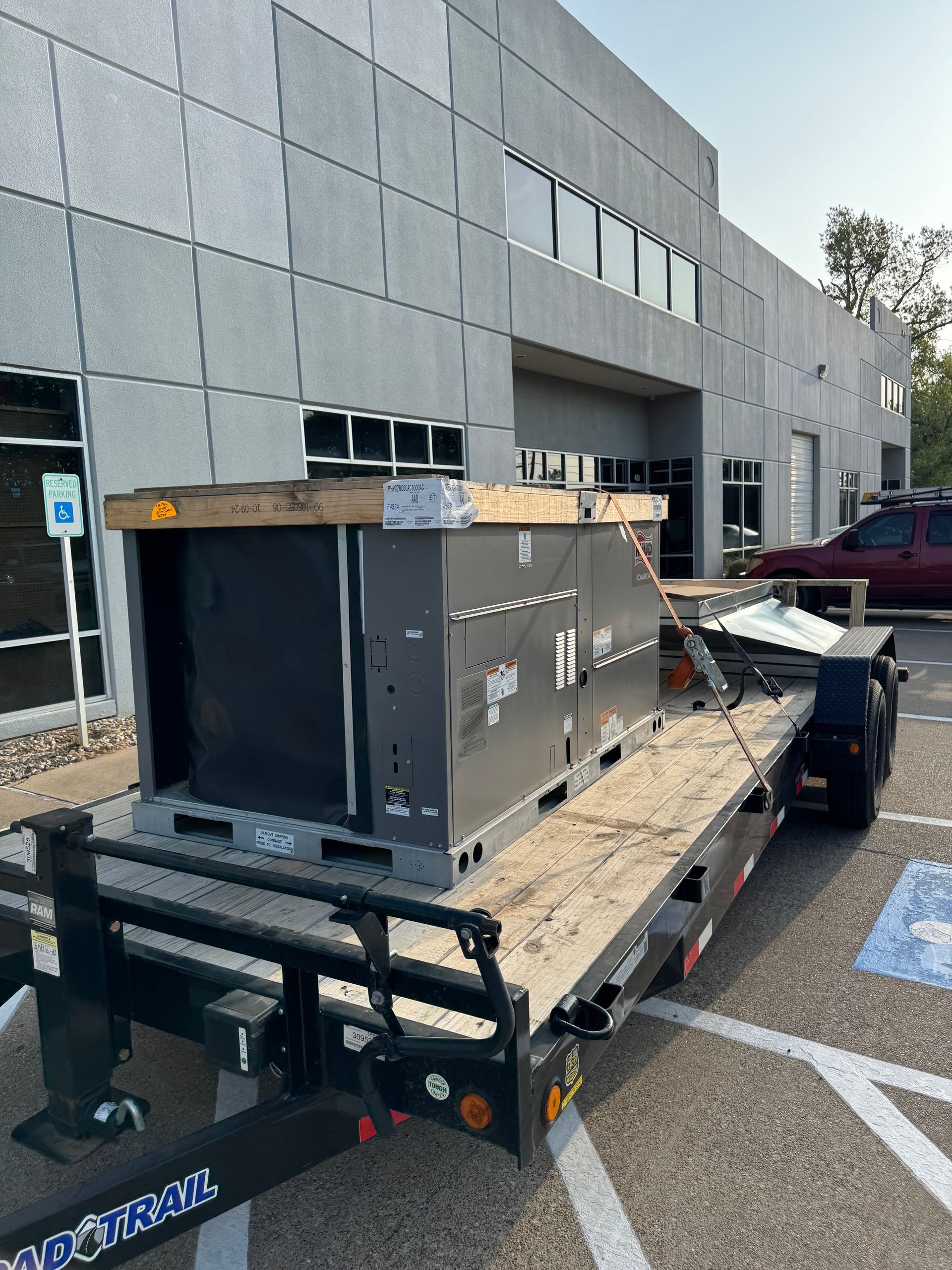 A large gray HVAC unit on a flatbed trailer in front of a modern building.