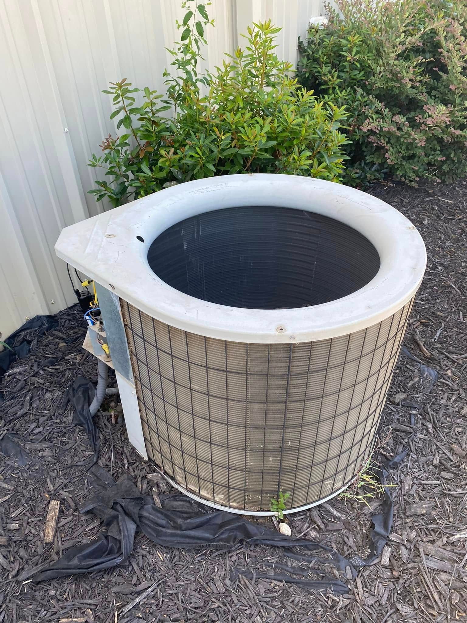 AC unit with visible interior, near a bush and wall.