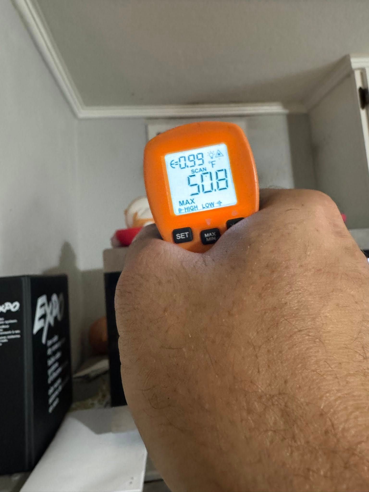 Person holding an orange temperature gun pointed at a wall, displaying a reading of 50.8 degrees.