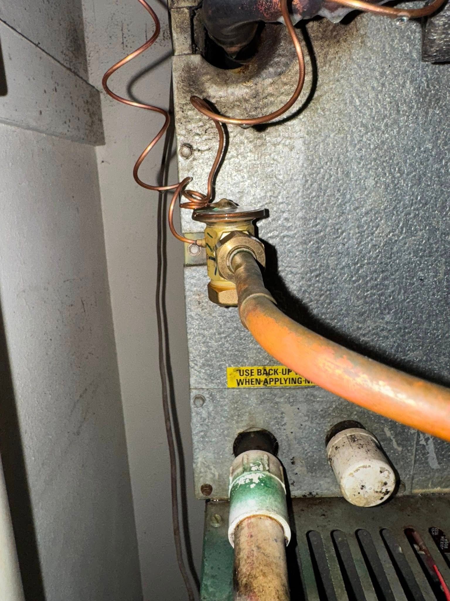 Copper pipes connected to a valve with a hose and a metal surface.