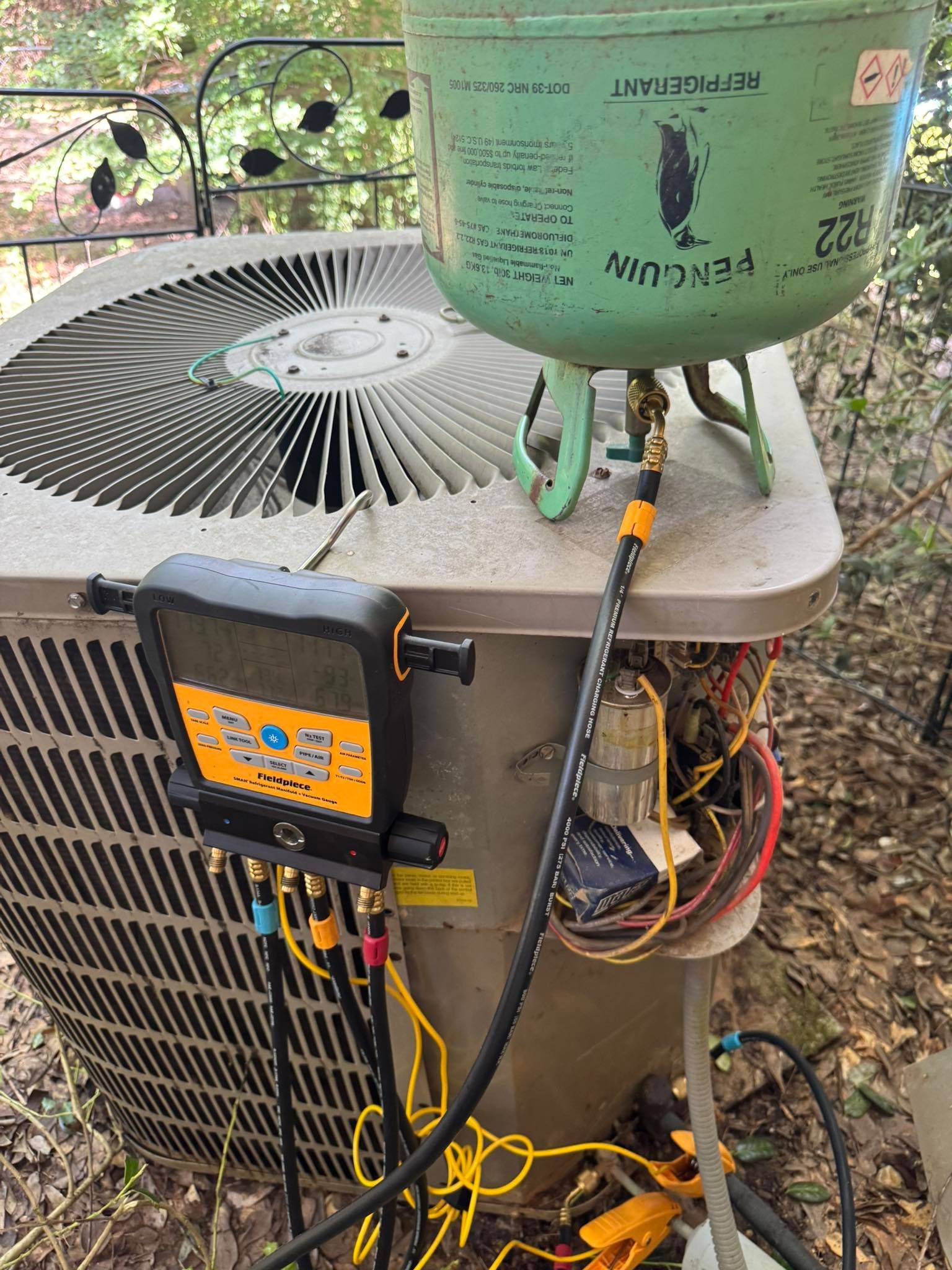AC unit being serviced with gauges and refrigerant tank, outdoors.
