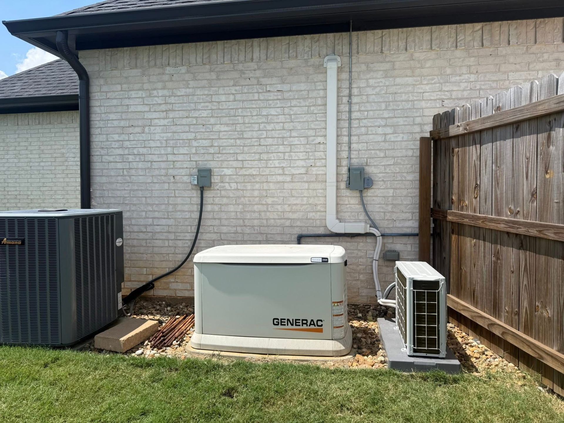 Exterior view of a generator and HVAC units next to a house with a brick wall and wooden fence.