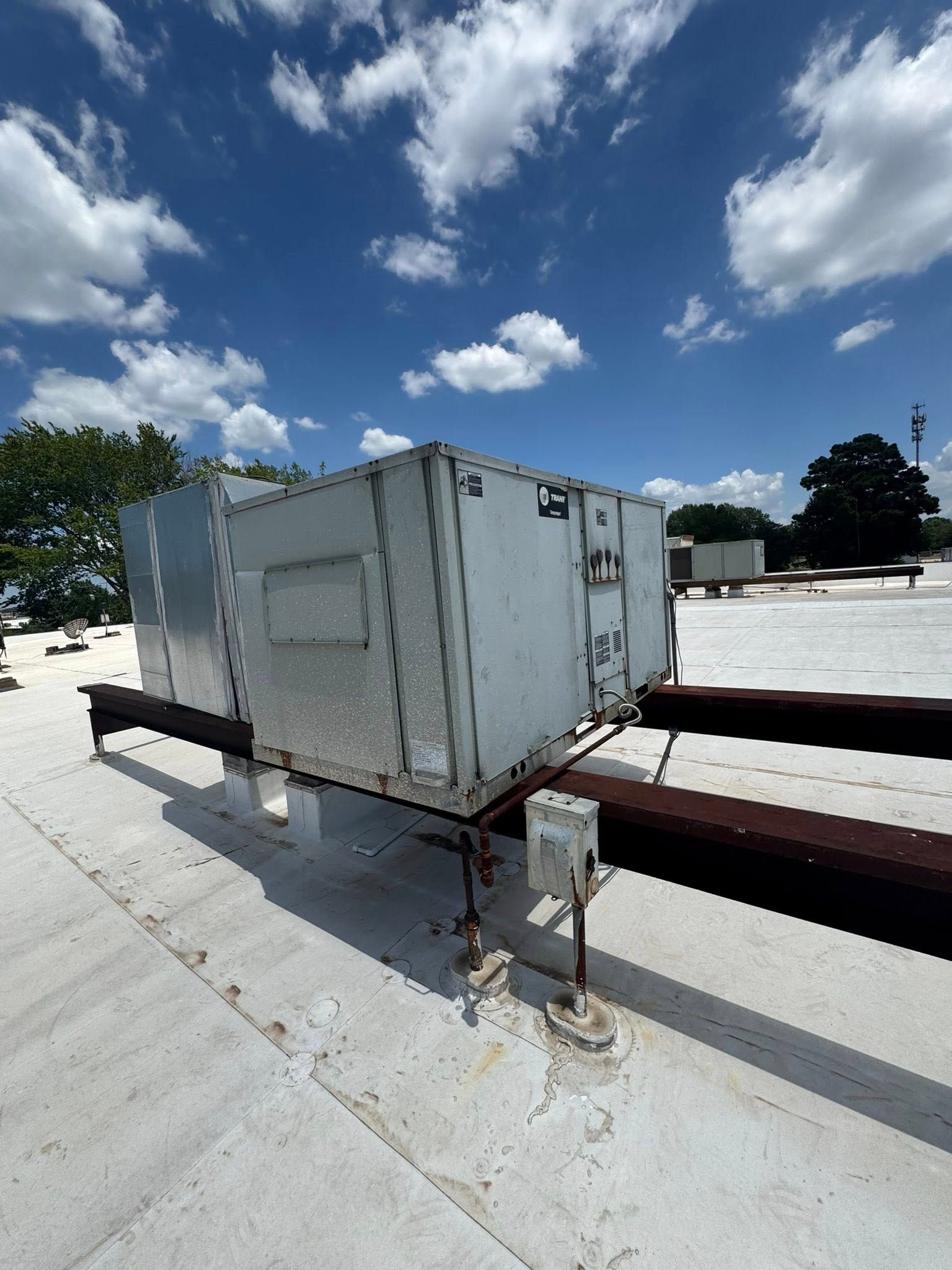 HVAC unit on a white roof against a blue sky with clouds. Metal structure.