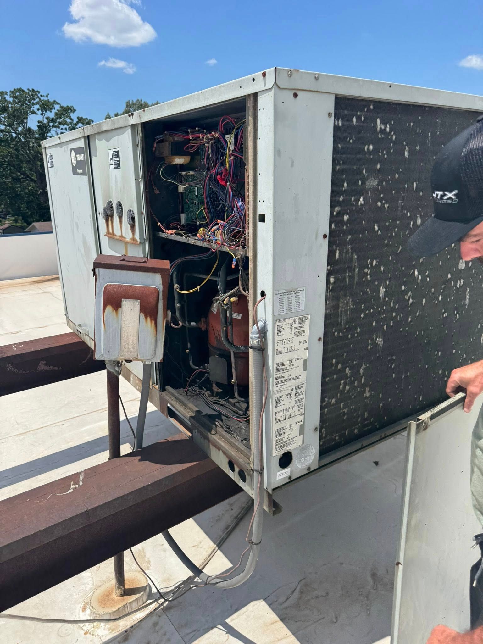 HVAC unit on a rooftop with exposed wiring; a person in the background, blue sky.