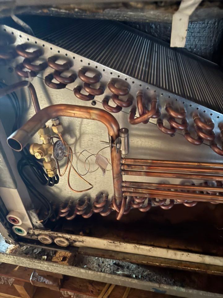 Close-up of air conditioning unit's copper coils, tubes, and valve within a metal housing.